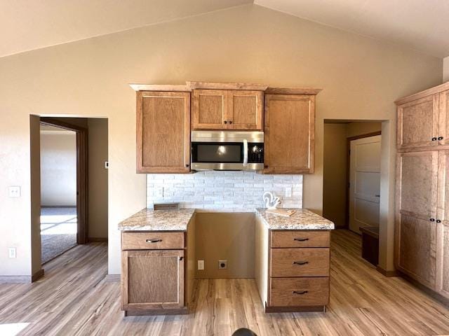 kitchen featuring vaulted ceiling, light hardwood / wood-style flooring, tasteful backsplash, and light stone countertops