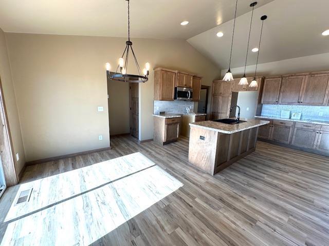 kitchen featuring sink, backsplash, a center island with sink, and hanging light fixtures