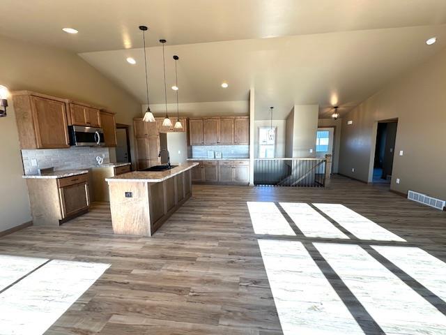 kitchen with tasteful backsplash, wood-type flooring, a kitchen island with sink, and pendant lighting