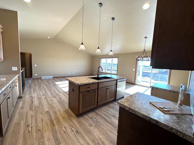 kitchen featuring decorative light fixtures, stainless steel dishwasher, sink, light stone countertops, and an island with sink