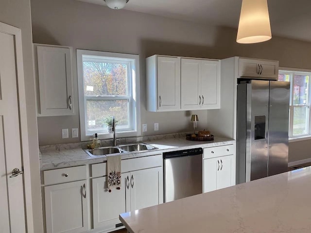 kitchen featuring white cabinetry, appliances with stainless steel finishes, hanging light fixtures, light stone counters, and sink