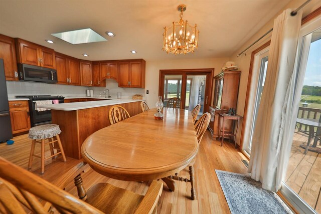 dining area featuring a skylight, sink, a chandelier, and light hardwood / wood-style floors