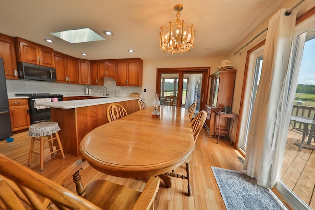 dining room featuring a skylight, sink, light hardwood / wood-style flooring, and an inviting chandelier