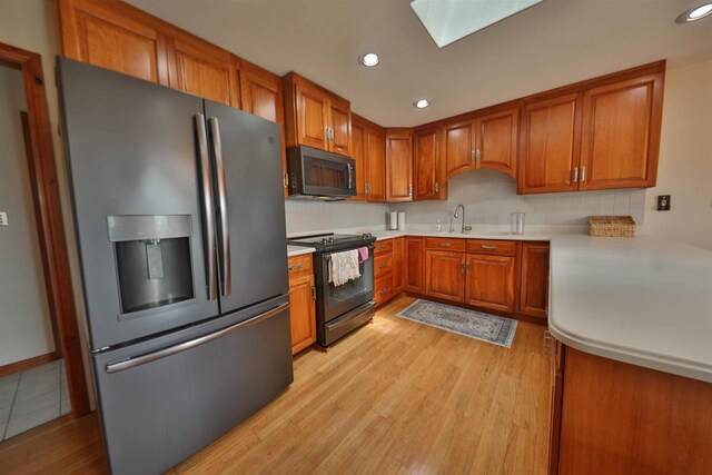 kitchen with stainless steel refrigerator with ice dispenser, a skylight, sink, electric range, and light hardwood / wood-style flooring