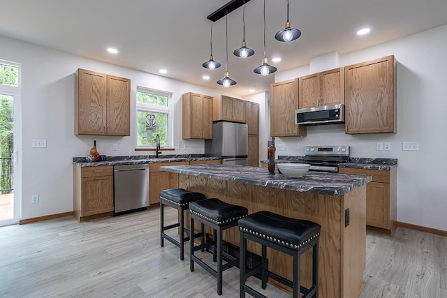 kitchen featuring stainless steel appliances, light wood-type flooring, pendant lighting, a breakfast bar, and a center island