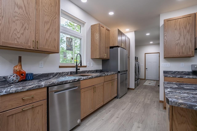 kitchen with stainless steel appliances, dark stone counters, light hardwood / wood-style flooring, washer / clothes dryer, and sink