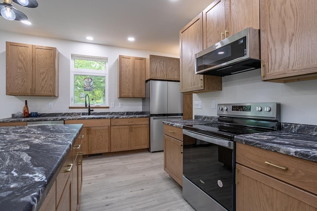 kitchen with sink, light hardwood / wood-style flooring, stainless steel appliances, and dark stone counters