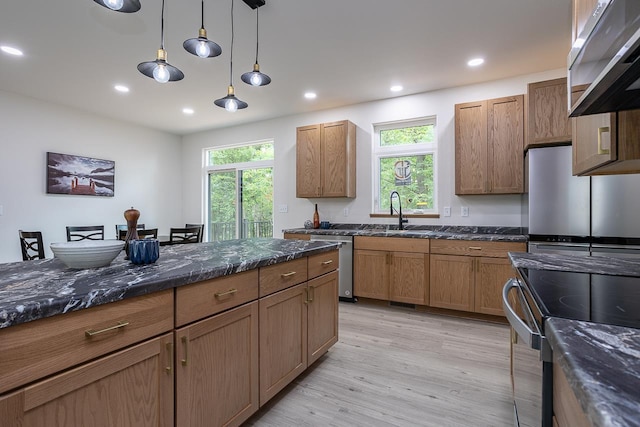 kitchen with pendant lighting, stainless steel appliances, dark stone counters, sink, and light hardwood / wood-style flooring