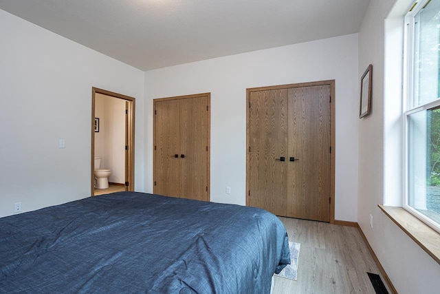 bedroom featuring light wood-type flooring, connected bathroom, and two closets