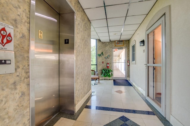 hall with tile patterned flooring, elevator, and a drop ceiling