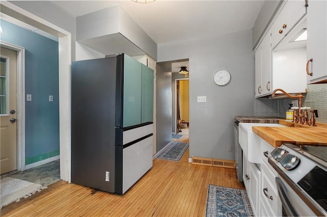 kitchen with tasteful backsplash, appliances with stainless steel finishes, white cabinets, and light hardwood / wood-style flooring