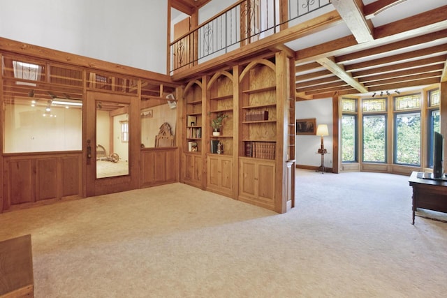 unfurnished living room with carpet, beam ceiling, wood walls, and built in shelves