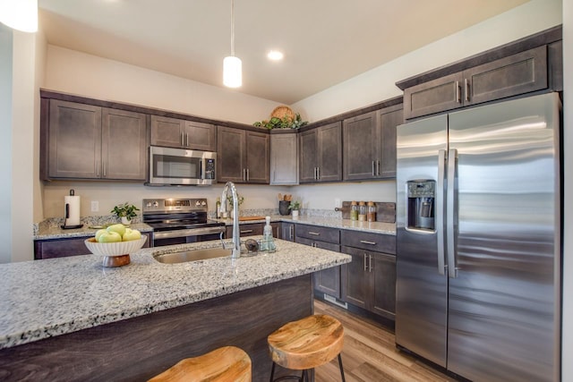 kitchen featuring appliances with stainless steel finishes, pendant lighting, light stone counters, and dark brown cabinetry