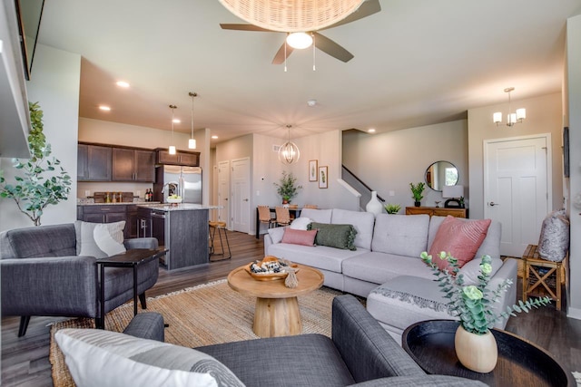 living room with ceiling fan with notable chandelier and dark hardwood / wood-style floors