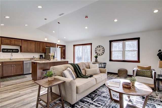 living room with sink, light wood-type flooring, and vaulted ceiling