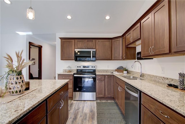 kitchen featuring stainless steel appliances, wood-type flooring, hanging light fixtures, light stone counters, and sink