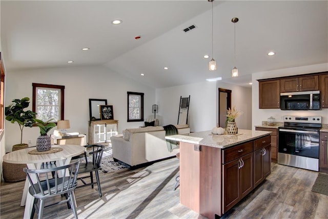 kitchen with appliances with stainless steel finishes, hanging light fixtures, vaulted ceiling, a kitchen island, and light stone counters