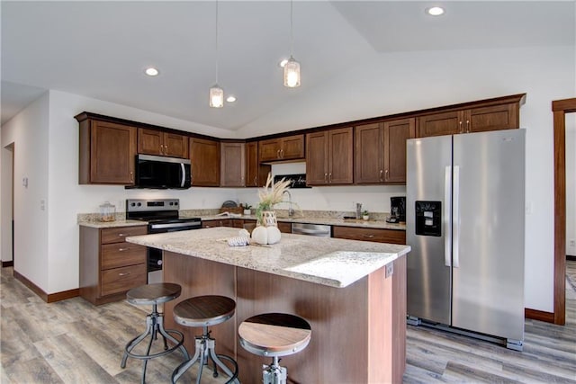 kitchen featuring appliances with stainless steel finishes, lofted ceiling, hanging light fixtures, light stone countertops, and a center island