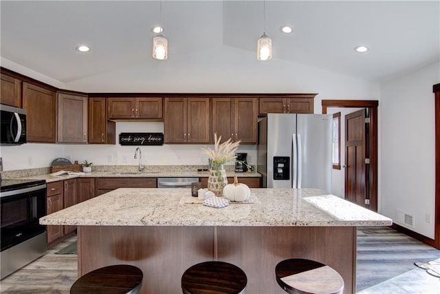 kitchen with appliances with stainless steel finishes, a kitchen island, wood-type flooring, sink, and hanging light fixtures