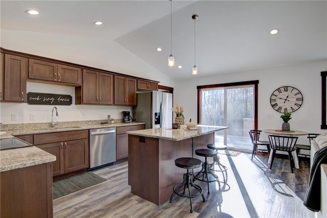 kitchen featuring appliances with stainless steel finishes, lofted ceiling, hanging light fixtures, a kitchen island, and sink