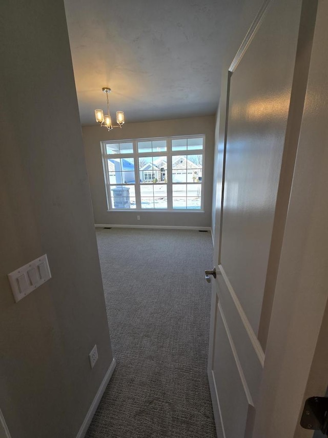 corridor featuring dark colored carpet and an inviting chandelier