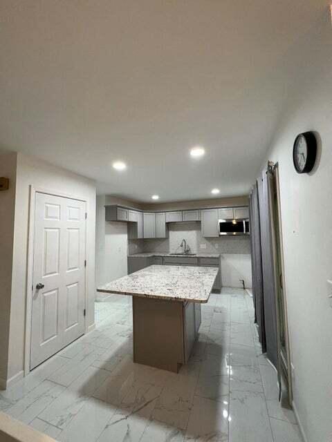 kitchen featuring light stone countertops, sink, gray cabinets, and a kitchen island