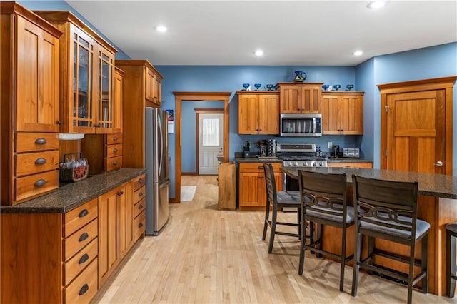 kitchen with light hardwood / wood-style flooring, stainless steel appliances, a kitchen breakfast bar, and dark stone counters