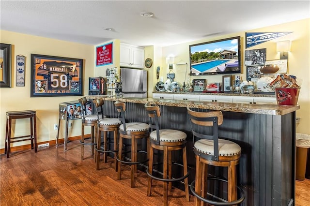 bar with dark wood-type flooring, stainless steel fridge, and white cabinets