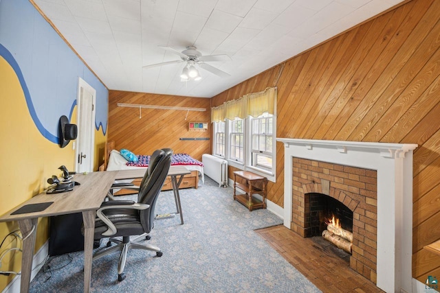 home office featuring ceiling fan, radiator heating unit, a fireplace, and wood walls