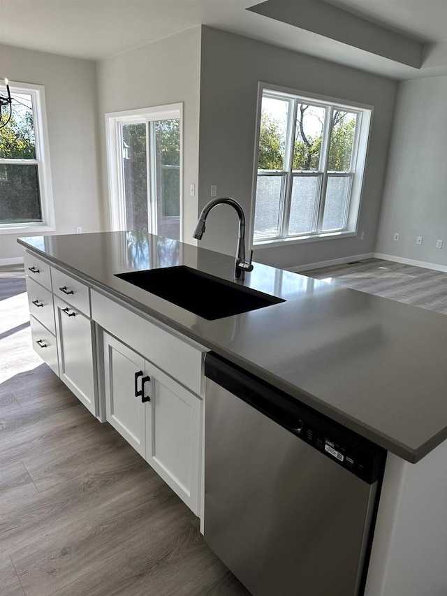 kitchen featuring sink, dishwasher, white cabinetry, wood-type flooring, and an island with sink