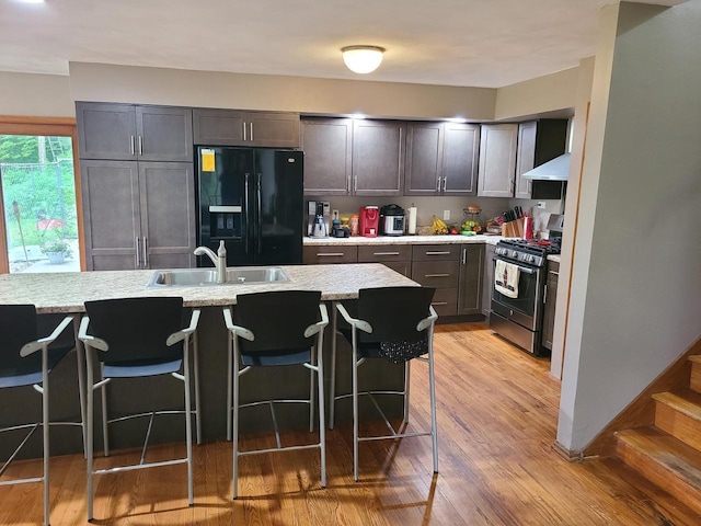 kitchen featuring black refrigerator with ice dispenser, light wood-style floors, gas stove, a sink, and a kitchen breakfast bar