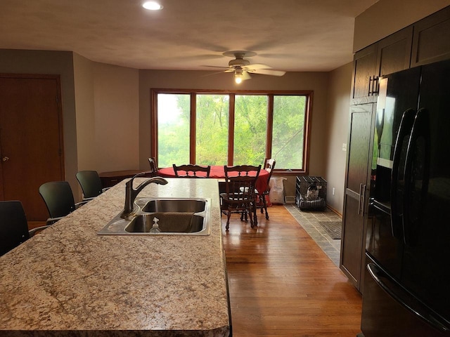 kitchen with an island with sink, light wood-style flooring, freestanding refrigerator, light stone countertops, and a sink