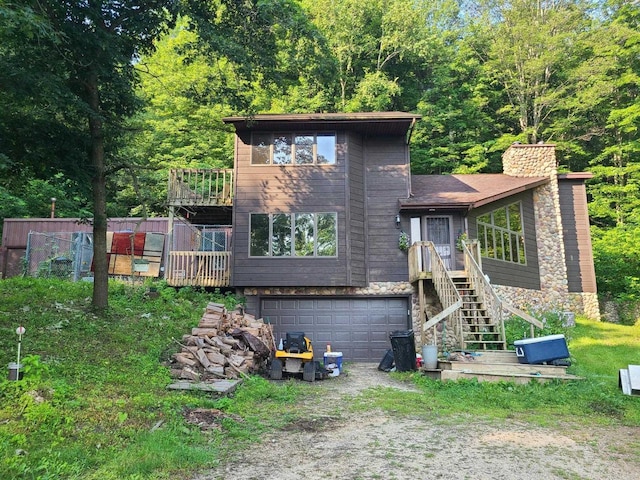 exterior space with an attached garage, dirt driveway, stone siding, a wooden deck, and a chimney