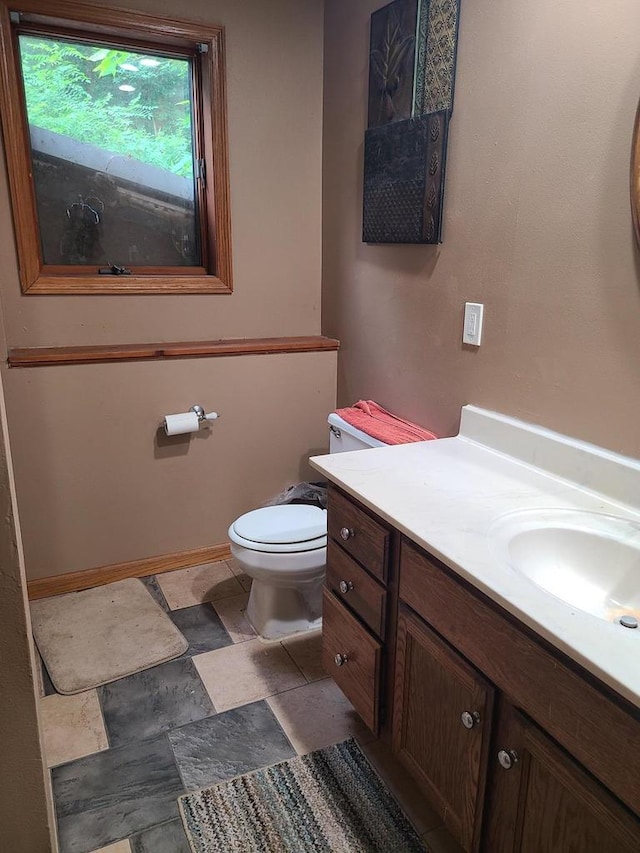 bathroom with stone finish floor, vanity, toilet, and baseboards