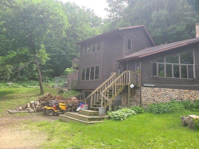 back of property featuring stone siding, stairway, and a lawn