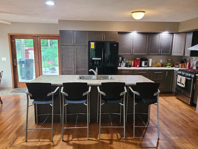 kitchen featuring stainless steel range with gas cooktop, a kitchen island with sink, a sink, a kitchen breakfast bar, and black fridge