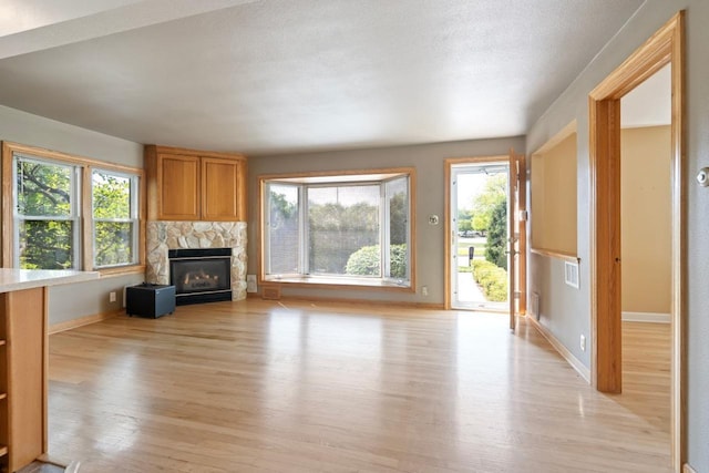 unfurnished living room featuring a stone fireplace, a wealth of natural light, a textured ceiling, and light hardwood / wood-style floors