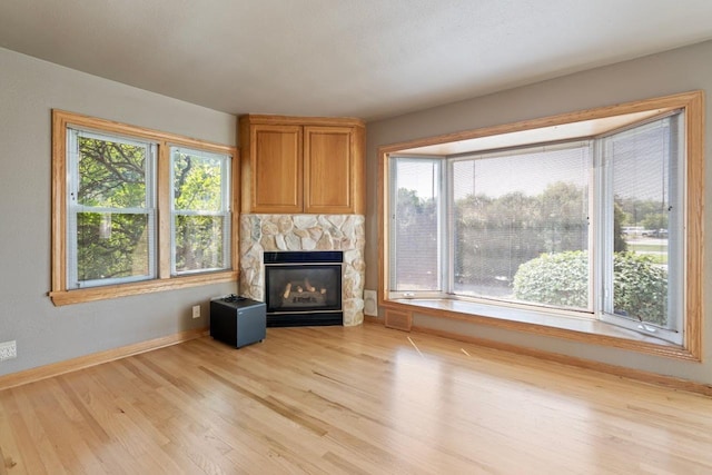 unfurnished living room with a stone fireplace and light wood-type flooring