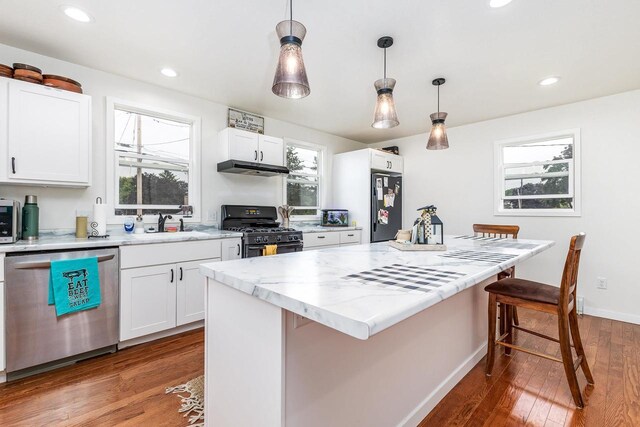 kitchen with hardwood / wood-style floors, double oven range, pendant lighting, stainless steel dishwasher, and white cabinetry