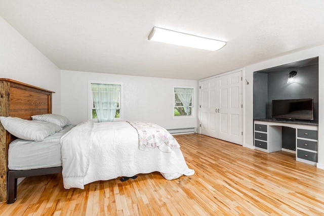 bedroom featuring light wood-type flooring, a baseboard heating unit, and a closet