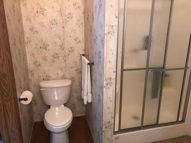 bathroom with hardwood / wood-style flooring, toilet, and a shower with shower door