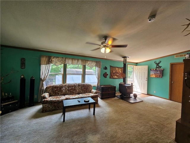 carpeted living room featuring ceiling fan, ornamental molding, a textured ceiling, and a wood stove