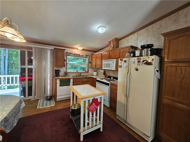 kitchen with crown molding, white appliances, lofted ceiling, and tile counters