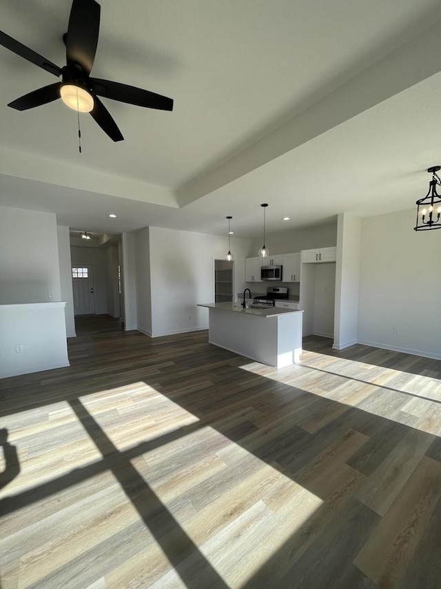 unfurnished living room with sink, ceiling fan with notable chandelier, and dark wood-type flooring