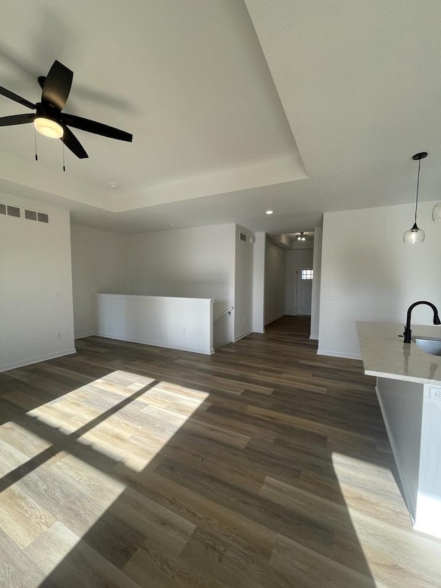 unfurnished living room with ceiling fan, dark hardwood / wood-style flooring, a raised ceiling, and sink