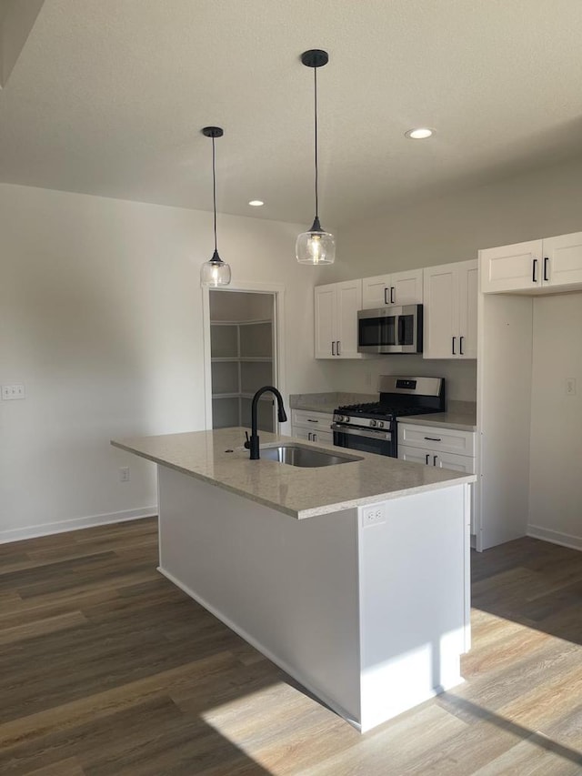 kitchen featuring decorative light fixtures, an island with sink, white cabinetry, sink, and stainless steel appliances