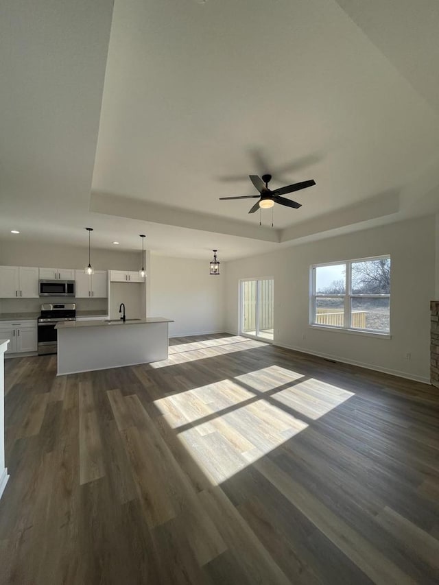 unfurnished living room featuring sink, dark wood-type flooring, ceiling fan, and a tray ceiling