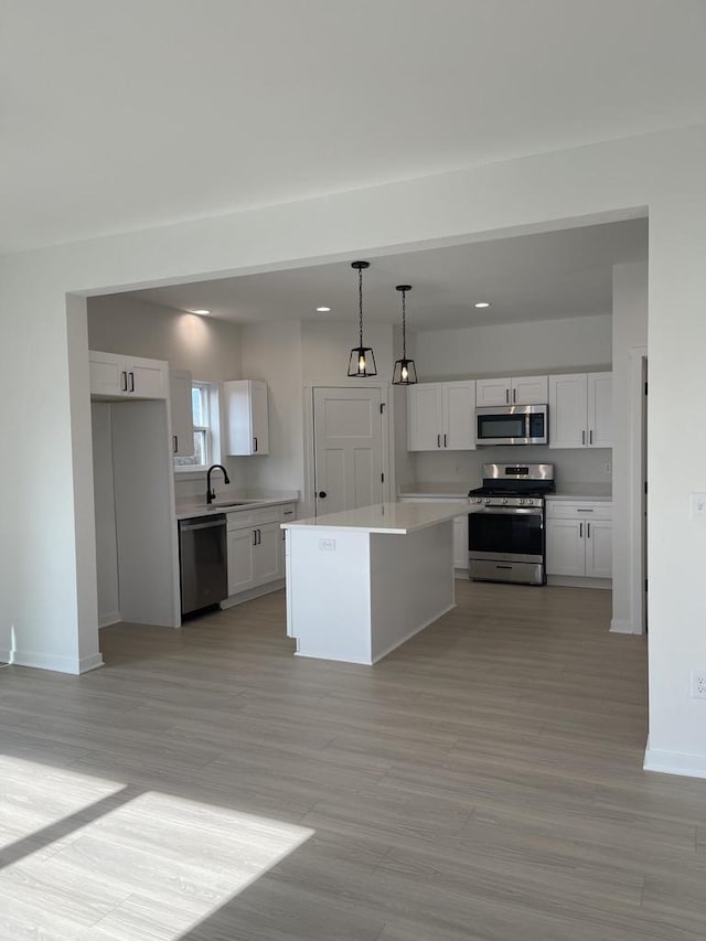 kitchen with decorative light fixtures, white cabinetry, sink, a center island, and stainless steel appliances