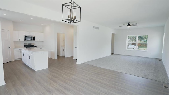 kitchen with a kitchen island, decorative light fixtures, white cabinets, stainless steel appliances, and light wood-type flooring