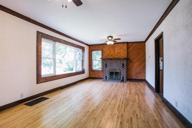 unfurnished living room featuring crown molding, ceiling fan, a fireplace, wood-type flooring, and wood walls